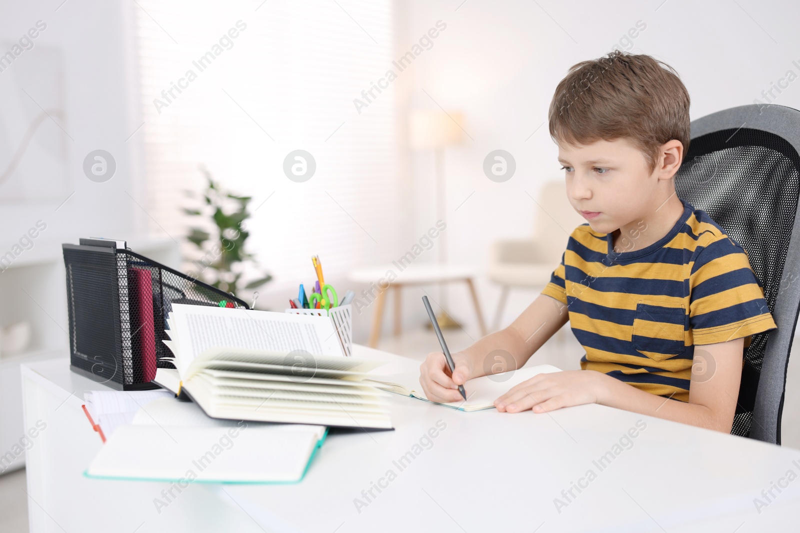 Photo of Boy with correct posture doing homework at white desk indoors