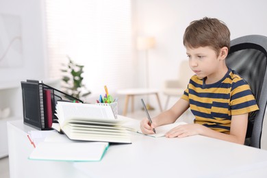 Boy with correct posture doing homework at white desk indoors