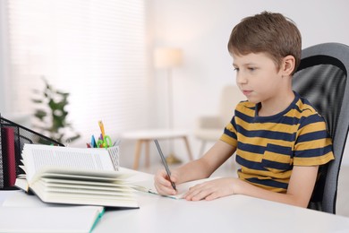 Photo of Boy with correct posture doing homework at white desk indoors