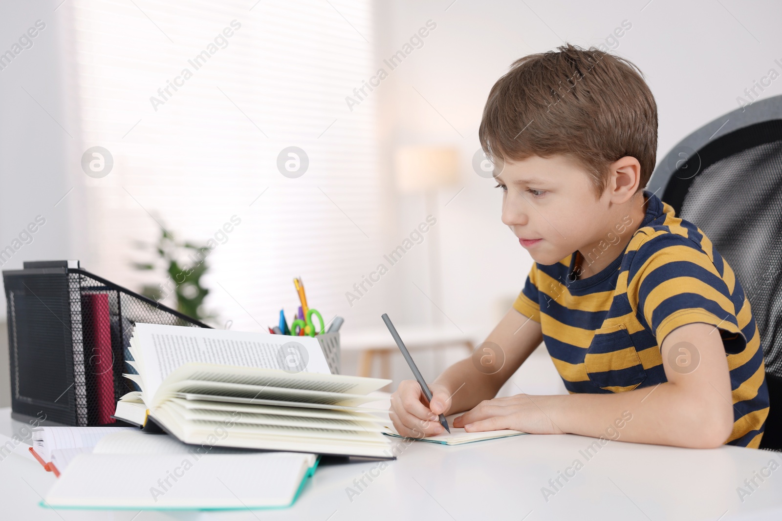 Photo of Boy with incorrect posture doing homework at white desk indoors