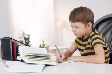 Photo of Boy with incorrect posture doing homework at white desk indoors