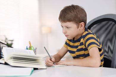 Photo of Boy with incorrect posture doing homework at white desk indoors