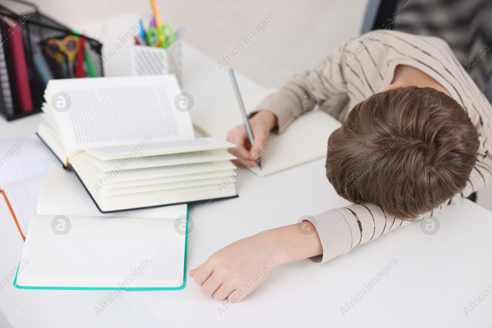 Photo of Boy with incorrect posture doing homework at white desk indoors