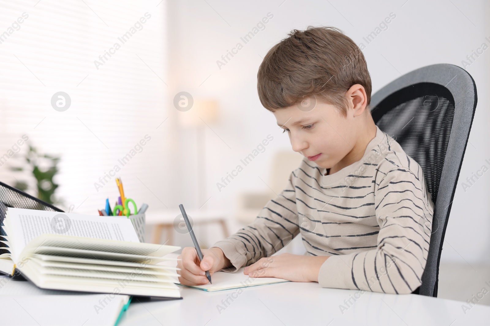 Photo of Boy with incorrect posture doing homework at white desk indoors