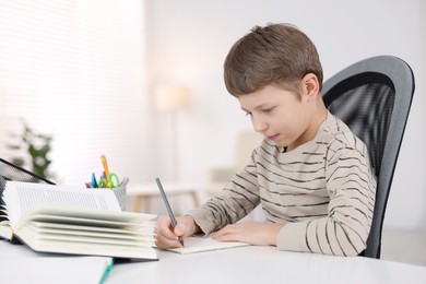 Boy with incorrect posture doing homework at white desk indoors