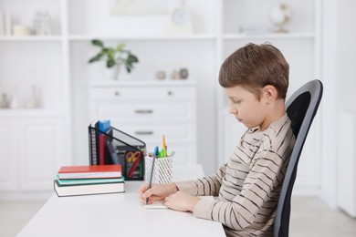 Boy with correct posture doing homework at white desk indoors