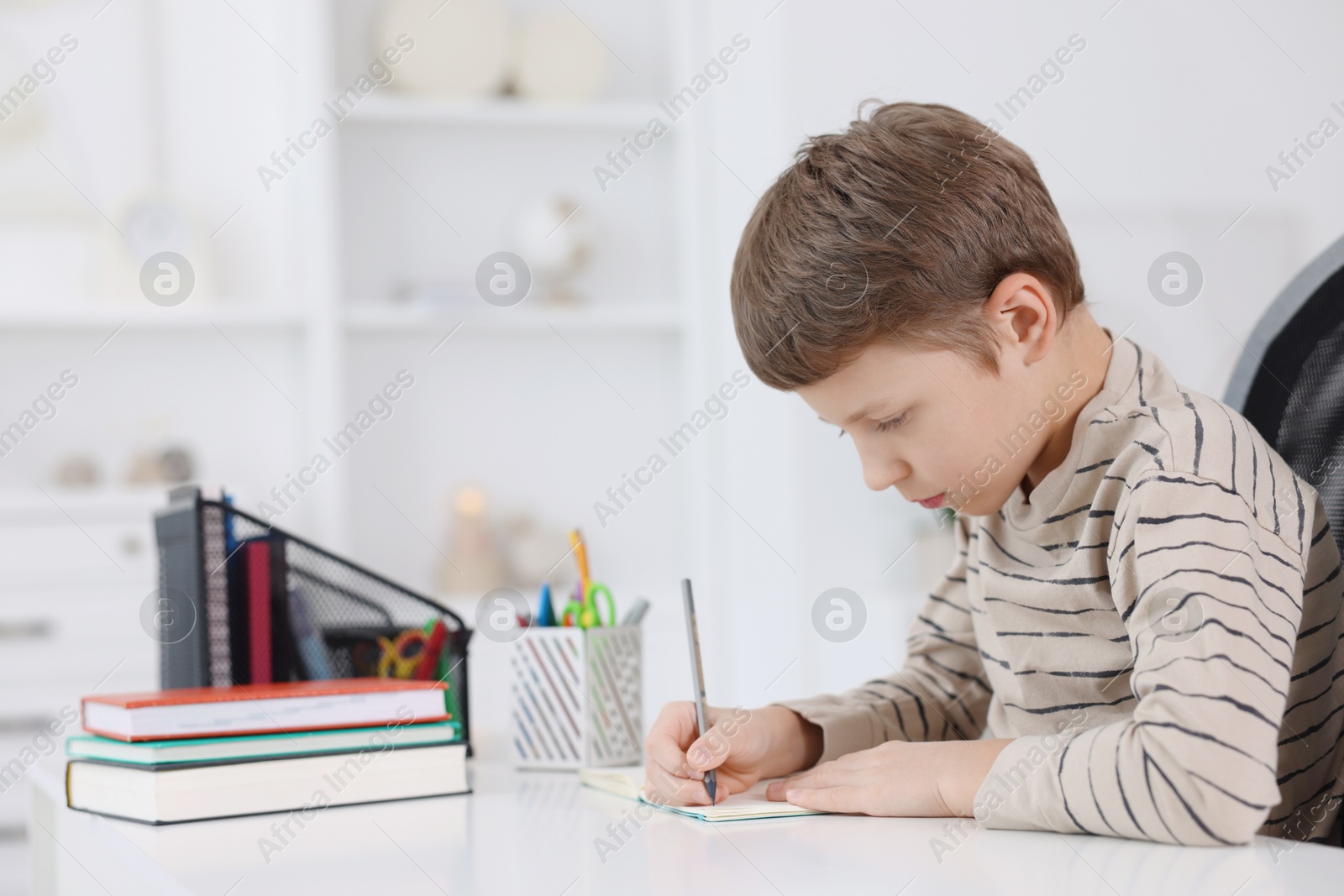 Photo of Boy with incorrect posture doing homework at white desk indoors