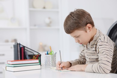 Photo of Boy with incorrect posture doing homework at white desk indoors