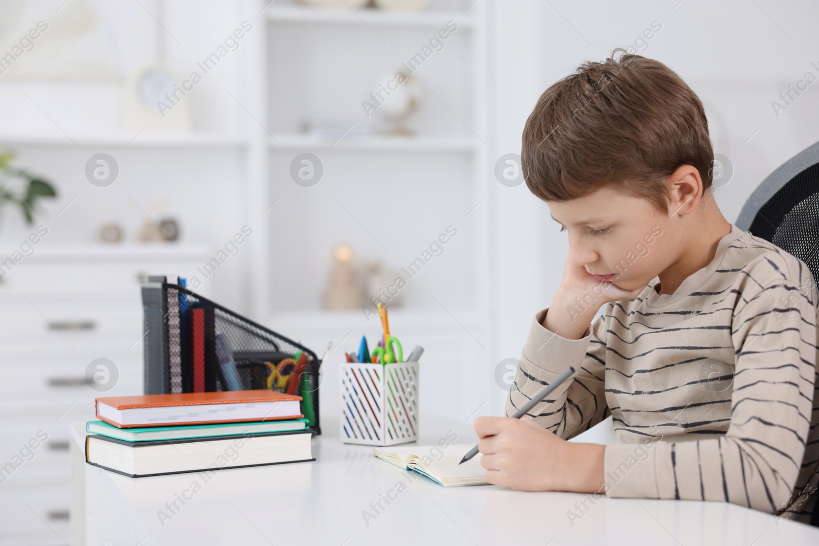 Photo of Boy with incorrect posture doing homework at white desk indoors