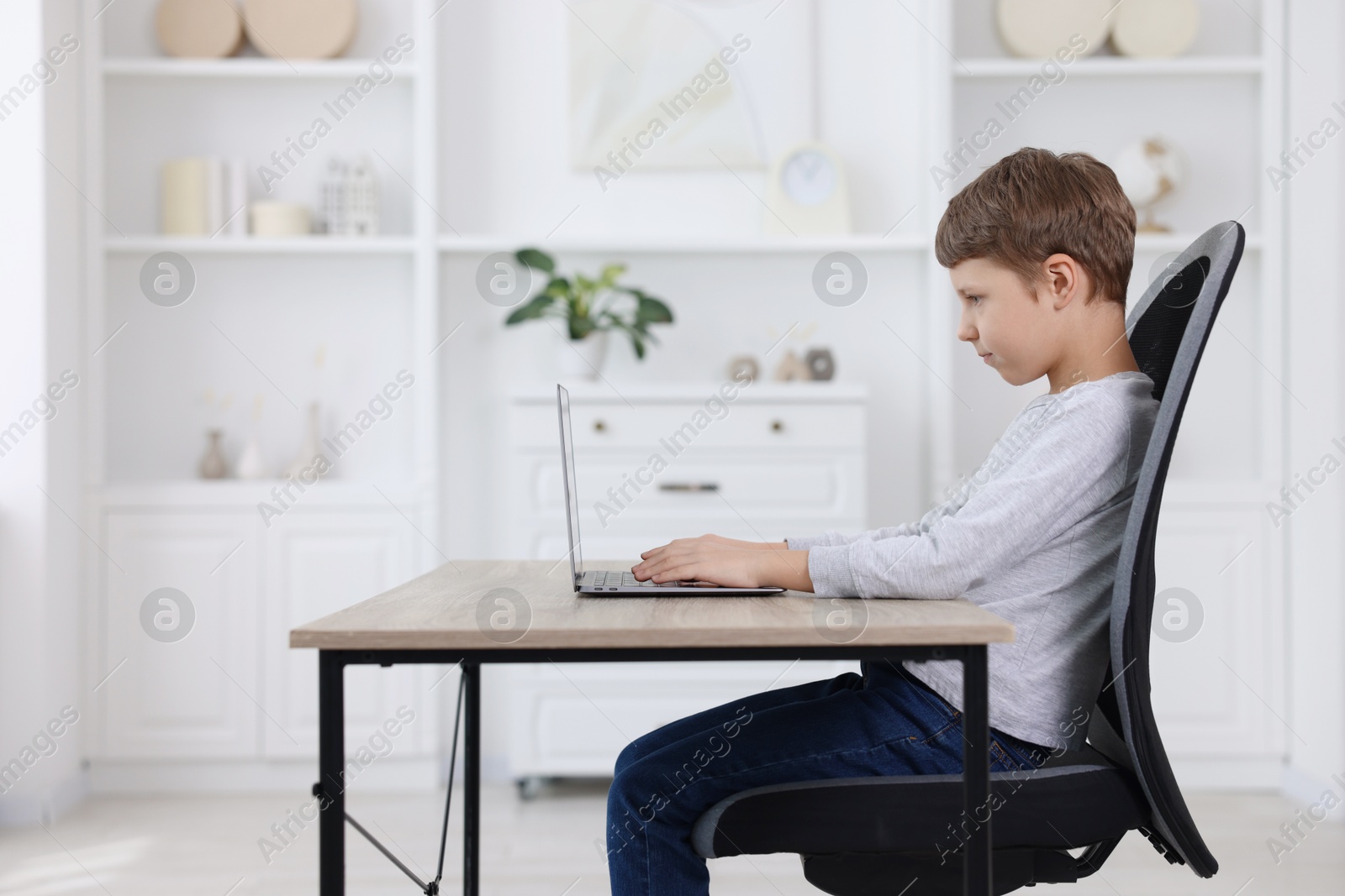 Photo of Boy with correct posture using laptop at wooden desk indoors