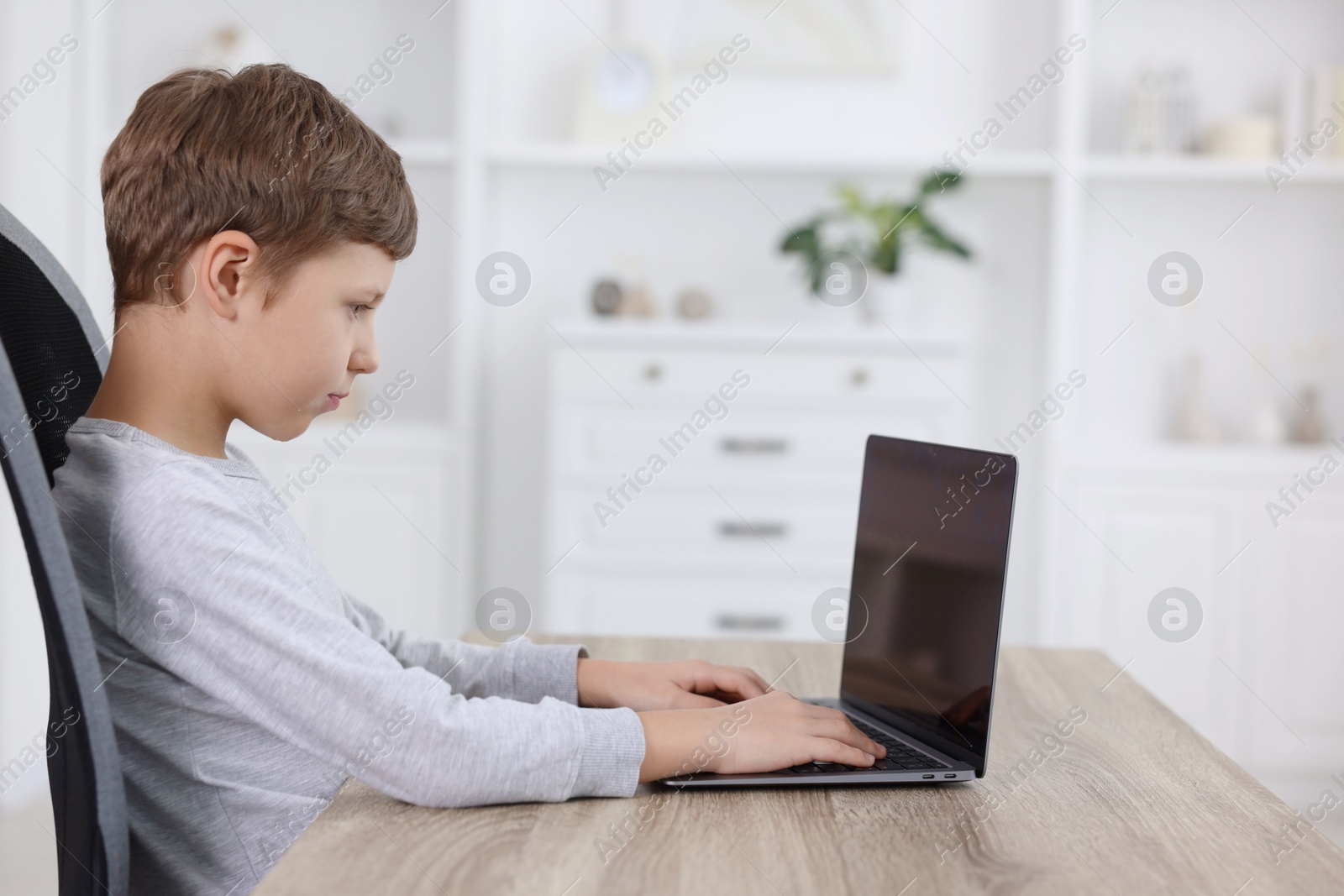 Photo of Boy with correct posture using laptop at wooden desk indoors