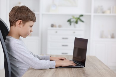 Boy with correct posture using laptop at wooden desk indoors