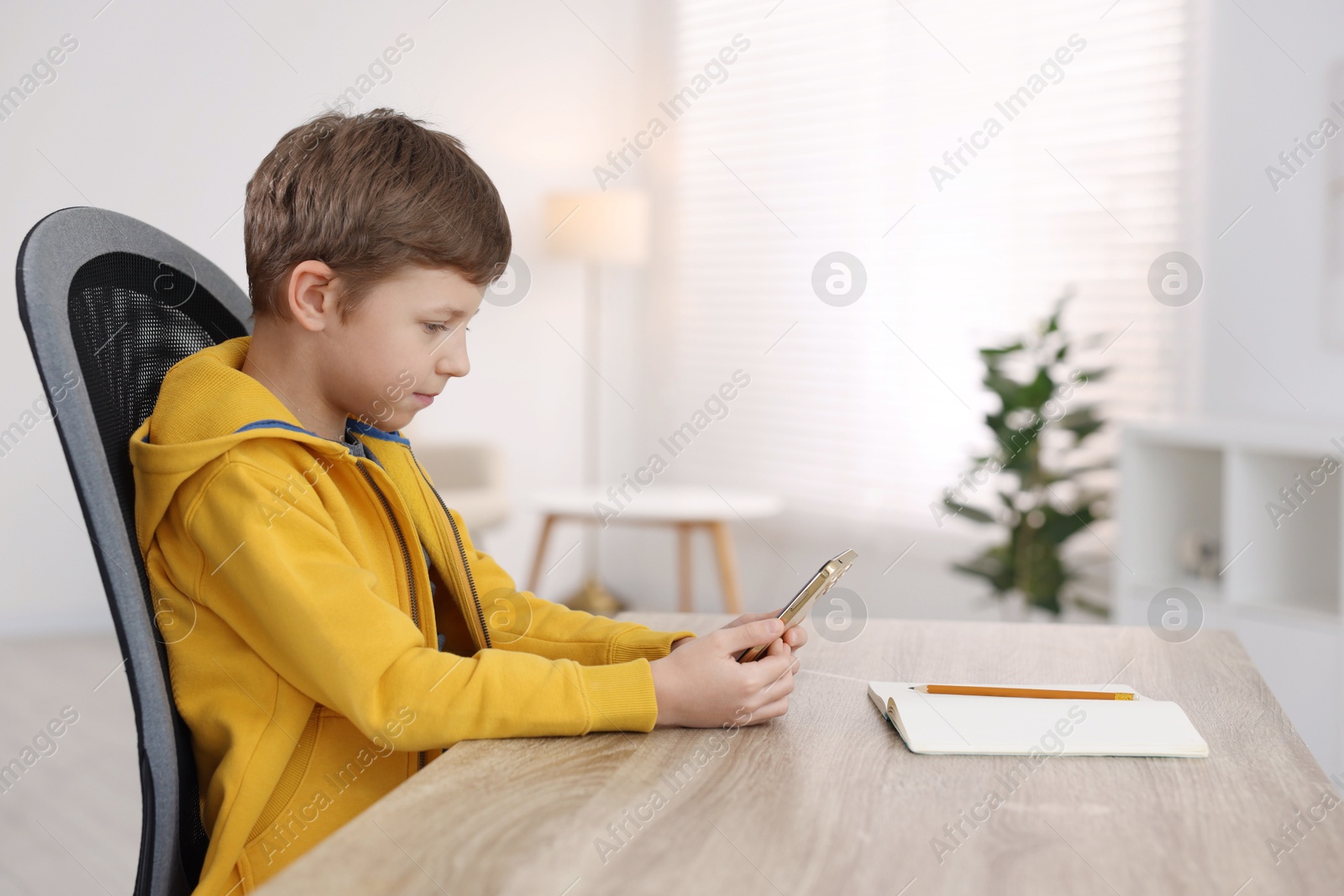 Photo of Boy with correct posture using smartphone at wooden desk indoors