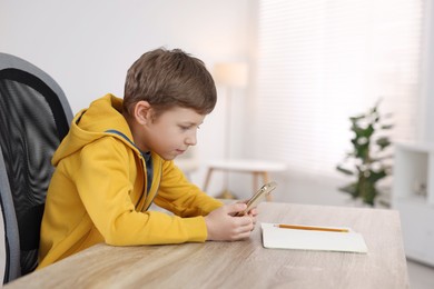 Photo of Boy with incorrect posture using laptop at wooden desk indoors