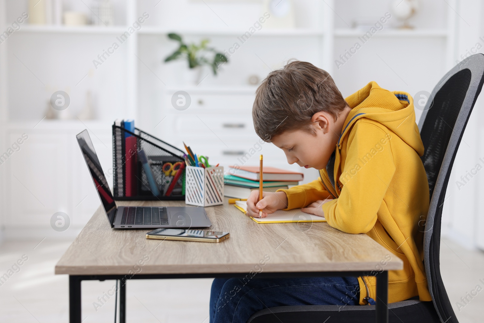 Photo of Boy with incorrect posture using laptop at wooden desk indoors