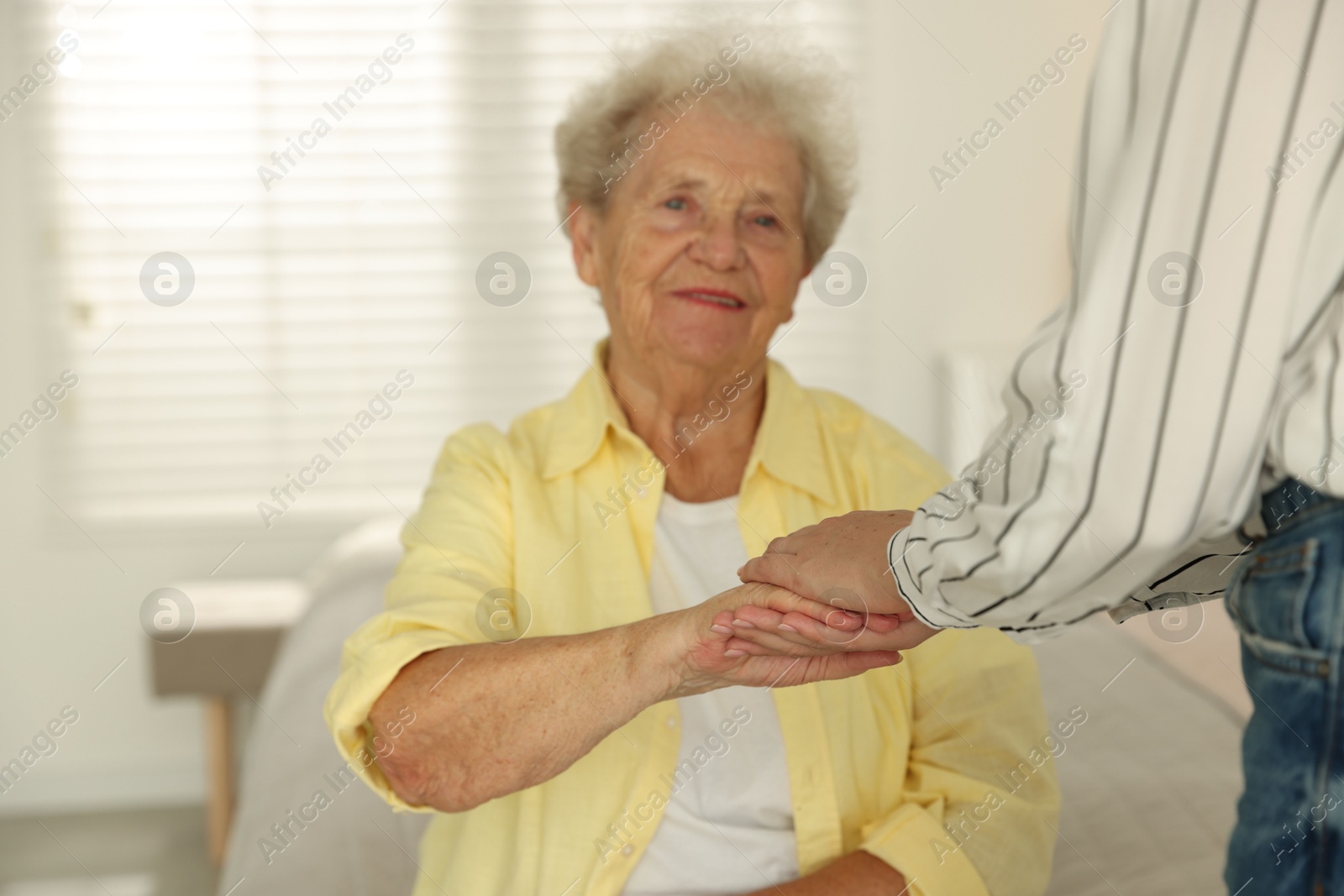 Photo of Senior woman holding hands with her granddaughter indoors, selective focus