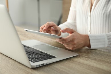 Photo of Businesswoman using tablet at wooden table indoors, closeup. Modern technology