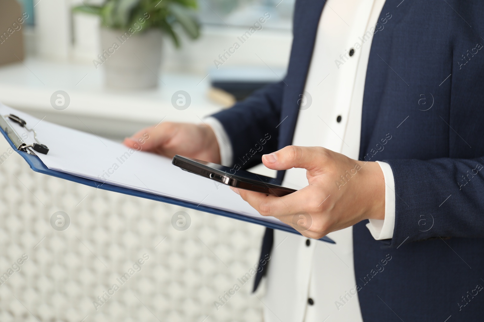 Photo of Businesswoman with clipboard using smartphone indoors, closeup. Modern technology