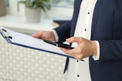 Photo of Businesswoman with clipboard using smartphone indoors, closeup. Modern technology