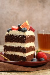 Photo of Piece of delicious chocolate sponge cake with berries and tea on wooden table, closeup