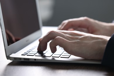 Photo of Businessman using laptop at table indoors, closeup. Modern technology