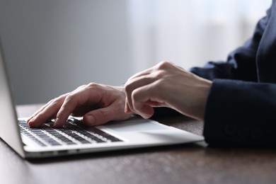 Photo of Businessman using laptop at table indoors, closeup. Modern technology