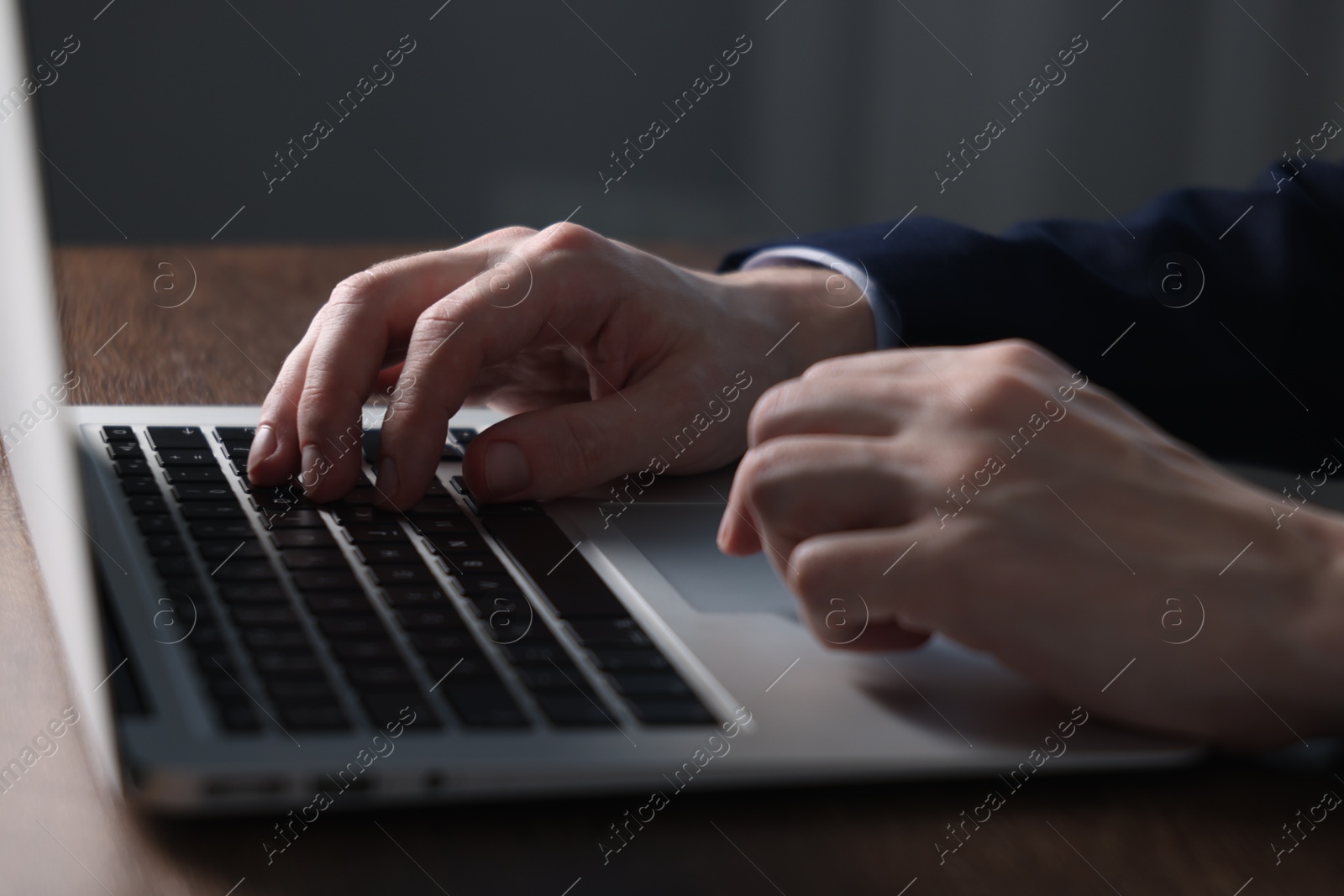 Photo of Businessman using laptop at wooden table indoors, closeup. Modern technology