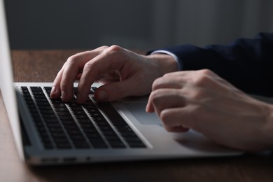 Photo of Businessman using laptop at wooden table indoors, closeup. Modern technology