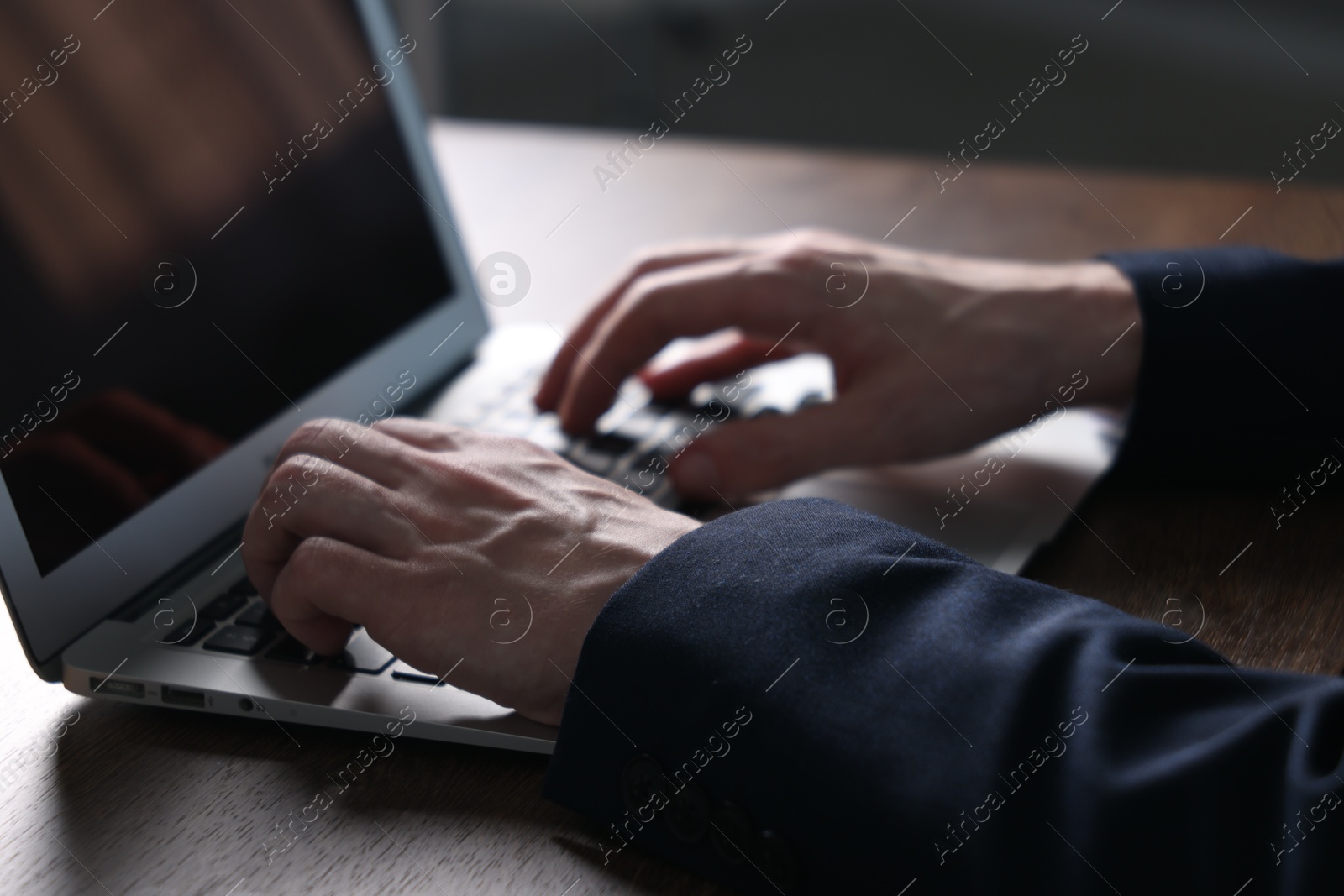 Photo of Businessman using laptop at wooden table indoors, closeup. Modern technology