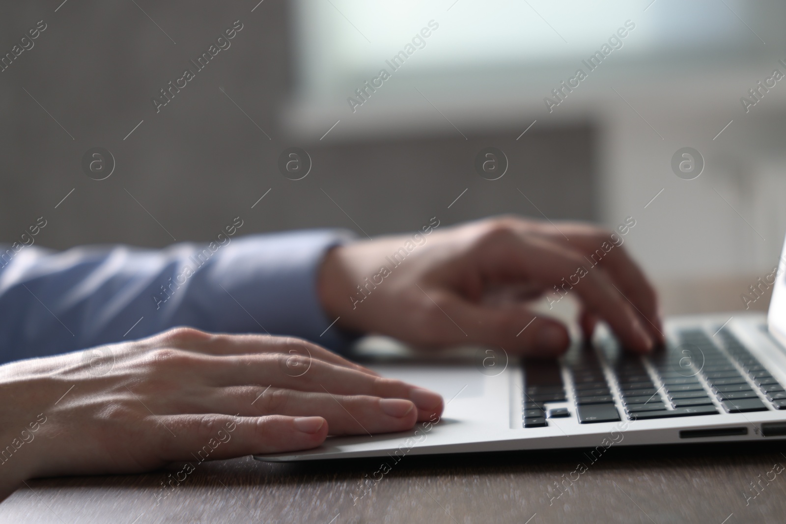 Photo of Businessman using laptop at wooden table indoors, closeup. Modern technology