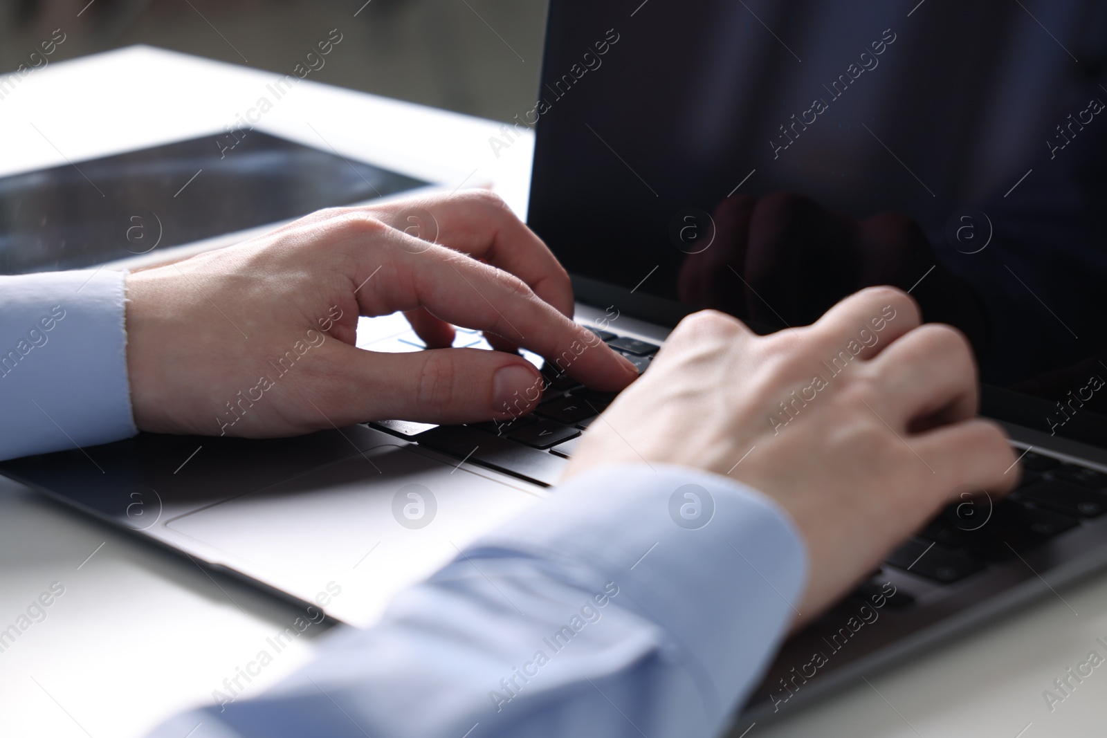 Photo of Businessman using laptop at white table indoors, closeup. Modern technology