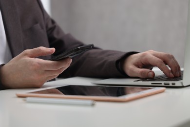 Photo of Businessman using different devices at white table indoors, closeup. Modern technology