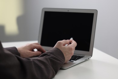 Photo of Businessman using laptop at white table indoors, closeup. Modern technology