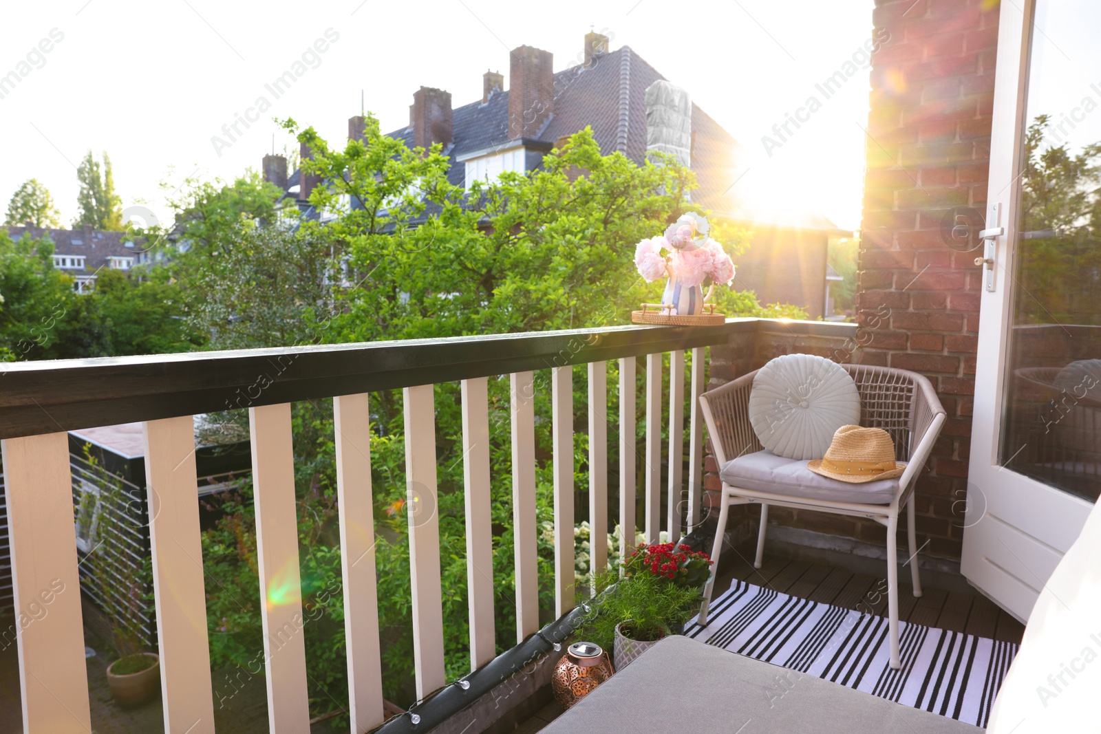 Photo of Vase with beautiful peonies on railings and chair at cozy balcony on sunny day