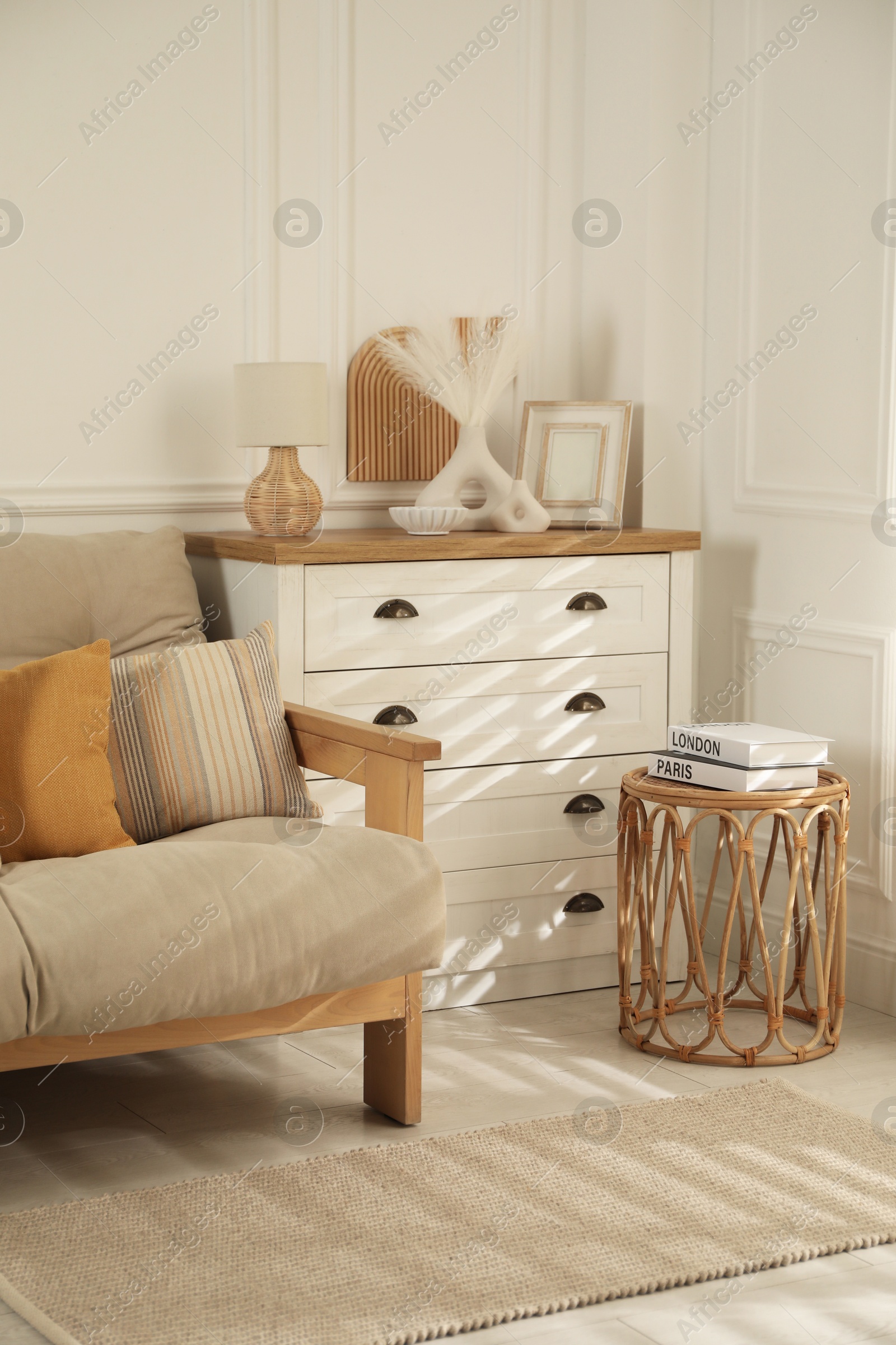 Photo of Sofa with soft pillows, chest of drawers, different decorative elements and side table indoors