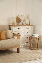 Sofa with soft pillows, chest of drawers, different decorative elements and side table indoors