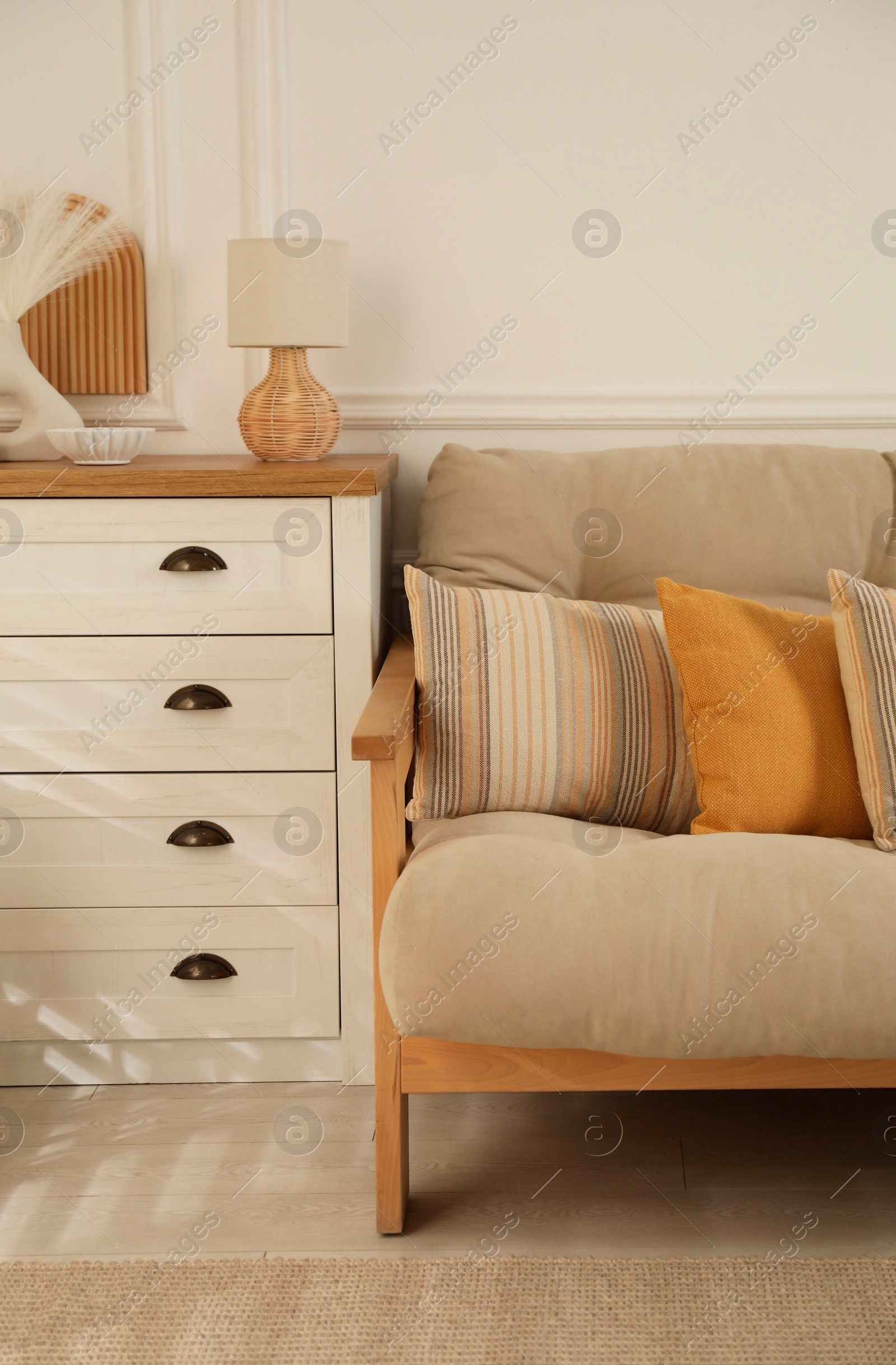 Photo of Sofa with soft pillows, chest of drawers and different decorative elements indoors