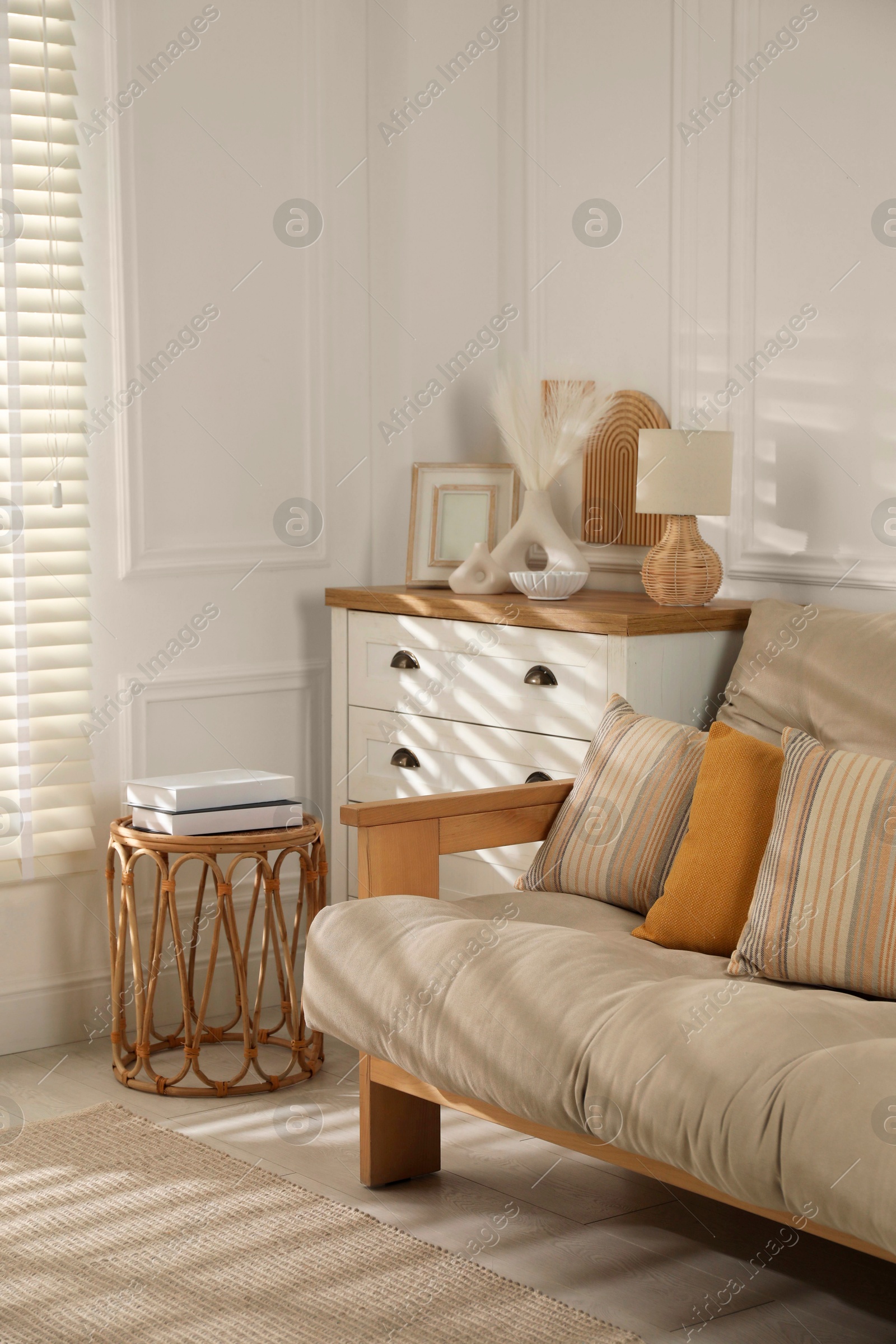 Photo of Sofa with soft pillows, chest of drawers, different decorative elements and side table indoors