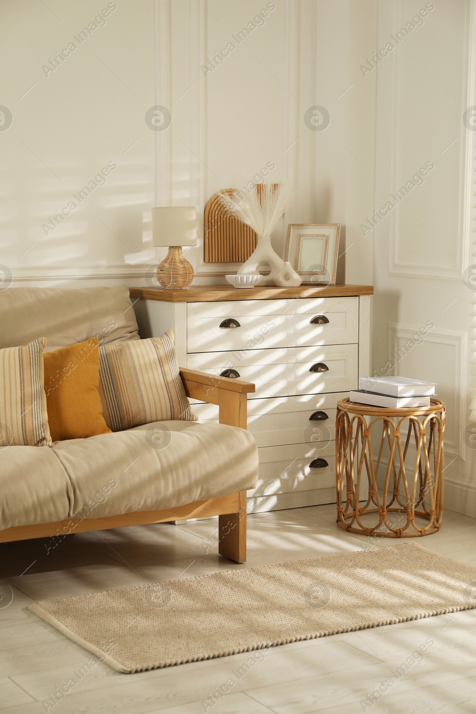 Photo of Sofa with soft pillows, chest of drawers, different decorative elements and side table indoors