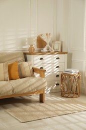 Photo of Sofa with soft pillows, chest of drawers, different decorative elements and side table indoors