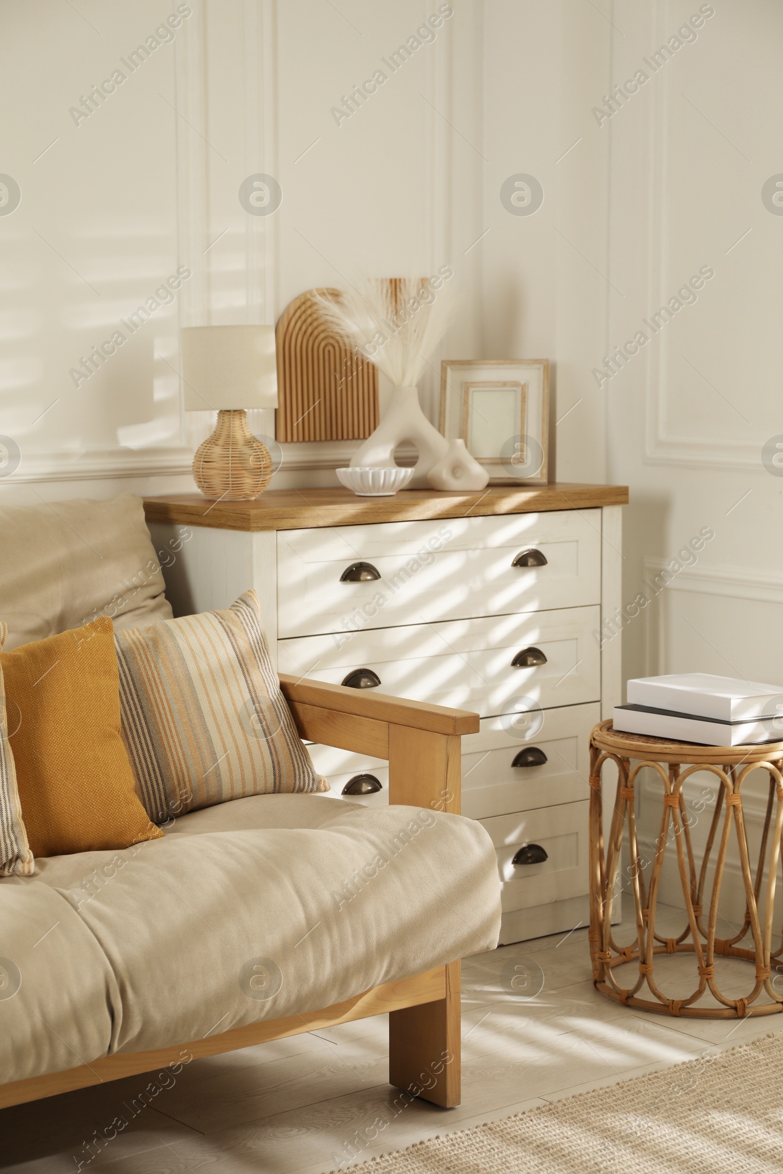 Photo of Sofa with soft pillows, chest of drawers, different decorative elements and side table indoors