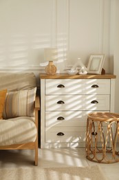 Photo of Sofa with soft pillows, chest of drawers, different decorative elements and side table indoors