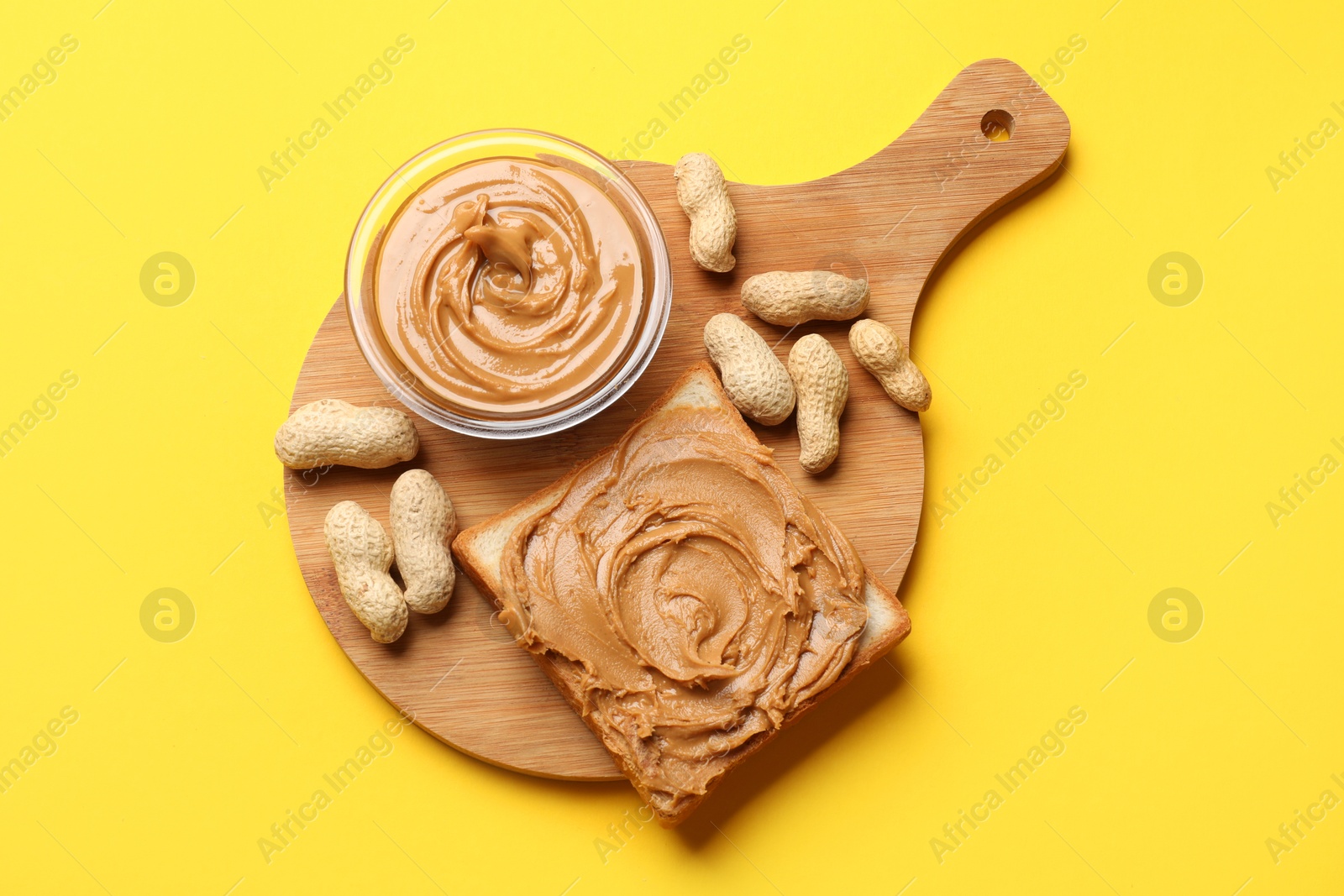 Photo of Delicious sandwich with peanut butter and fresh nuts on yellow table, top view