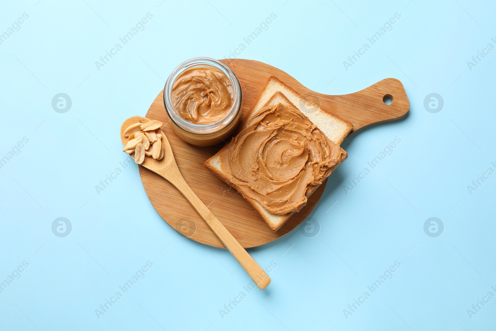 Photo of Delicious sandwich with peanut butter and fresh nuts on light blue table, top view