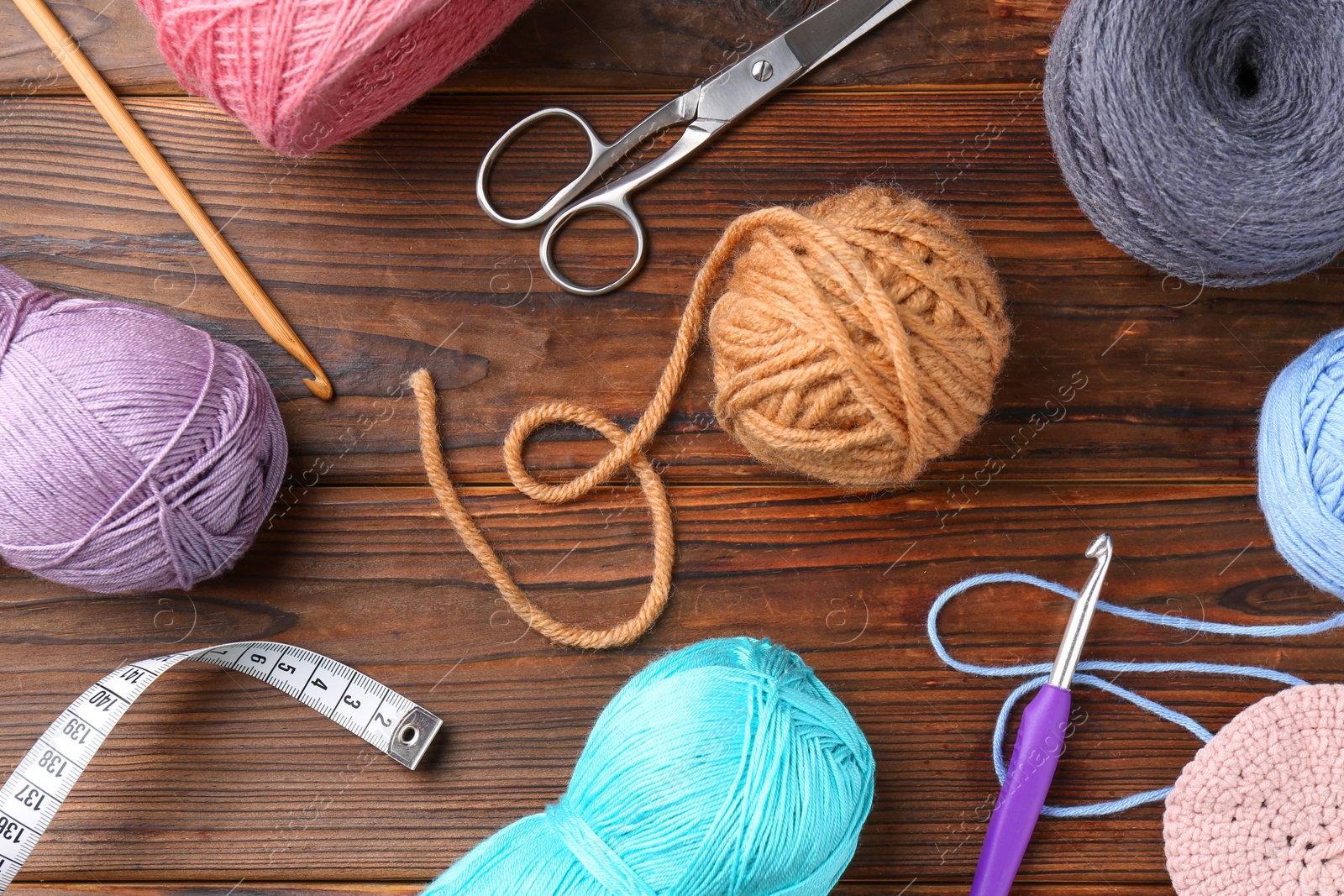 Photo of Colorful yarns, crochet hooks and other tools on wooden table, flat lay