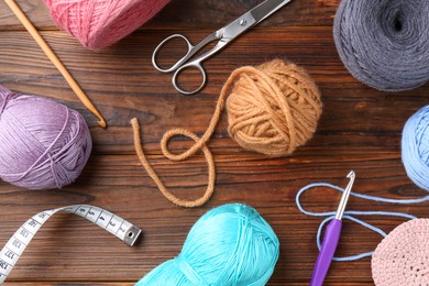 Photo of Colorful yarns, crochet hooks and other tools on wooden table, flat lay