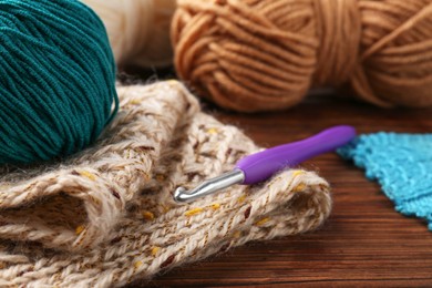 Photo of Crochet hook, sweater and yarn on wooden table, closeup