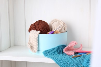 Photo of Different yarns, pattern samples and crochet hooks on white shelf