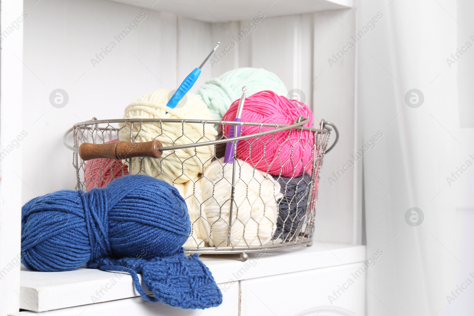 Photo of Different yarns, pattern samples and crochet hooks on white shelf