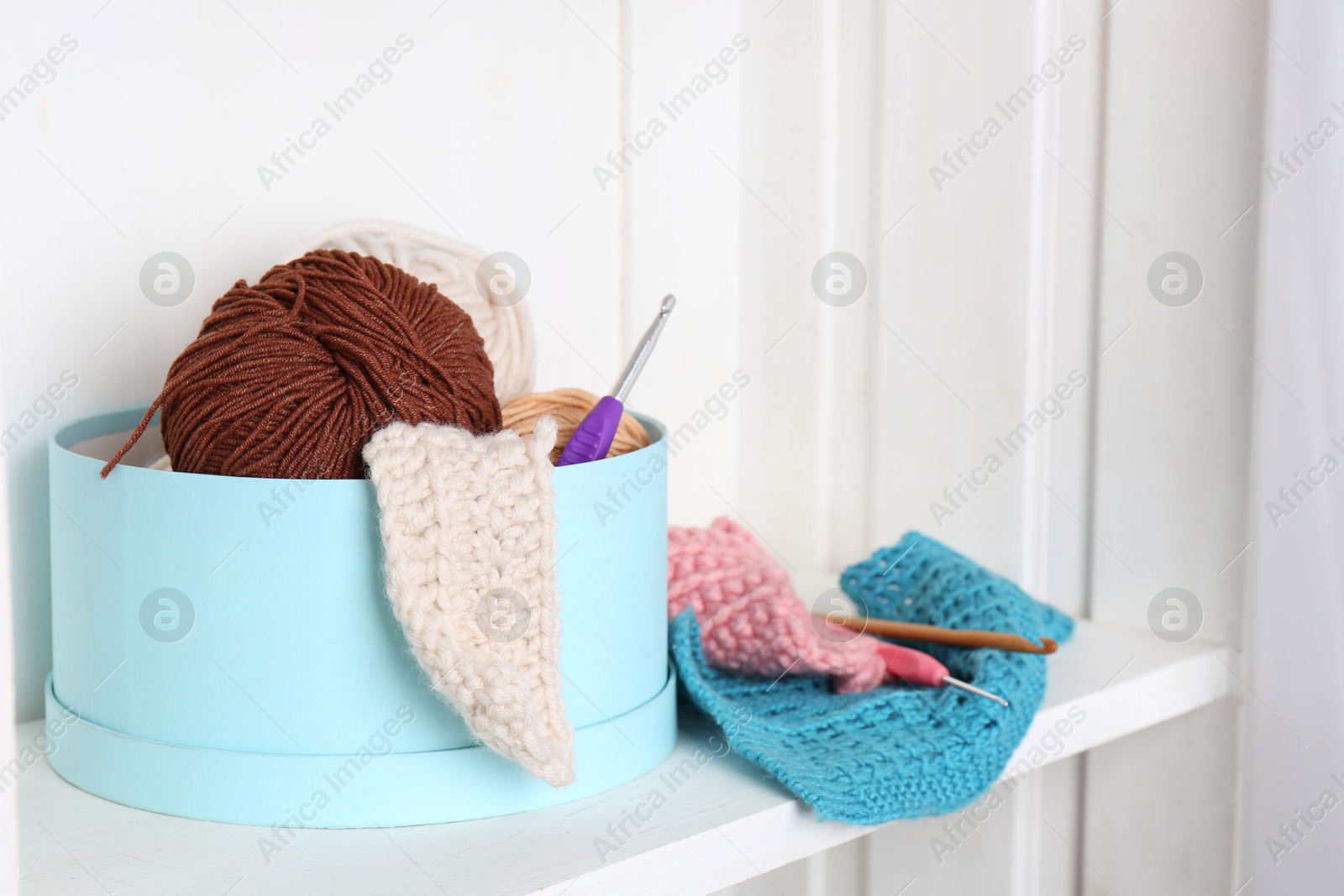 Photo of Different yarns, pattern samples and crochet hooks on white shelf